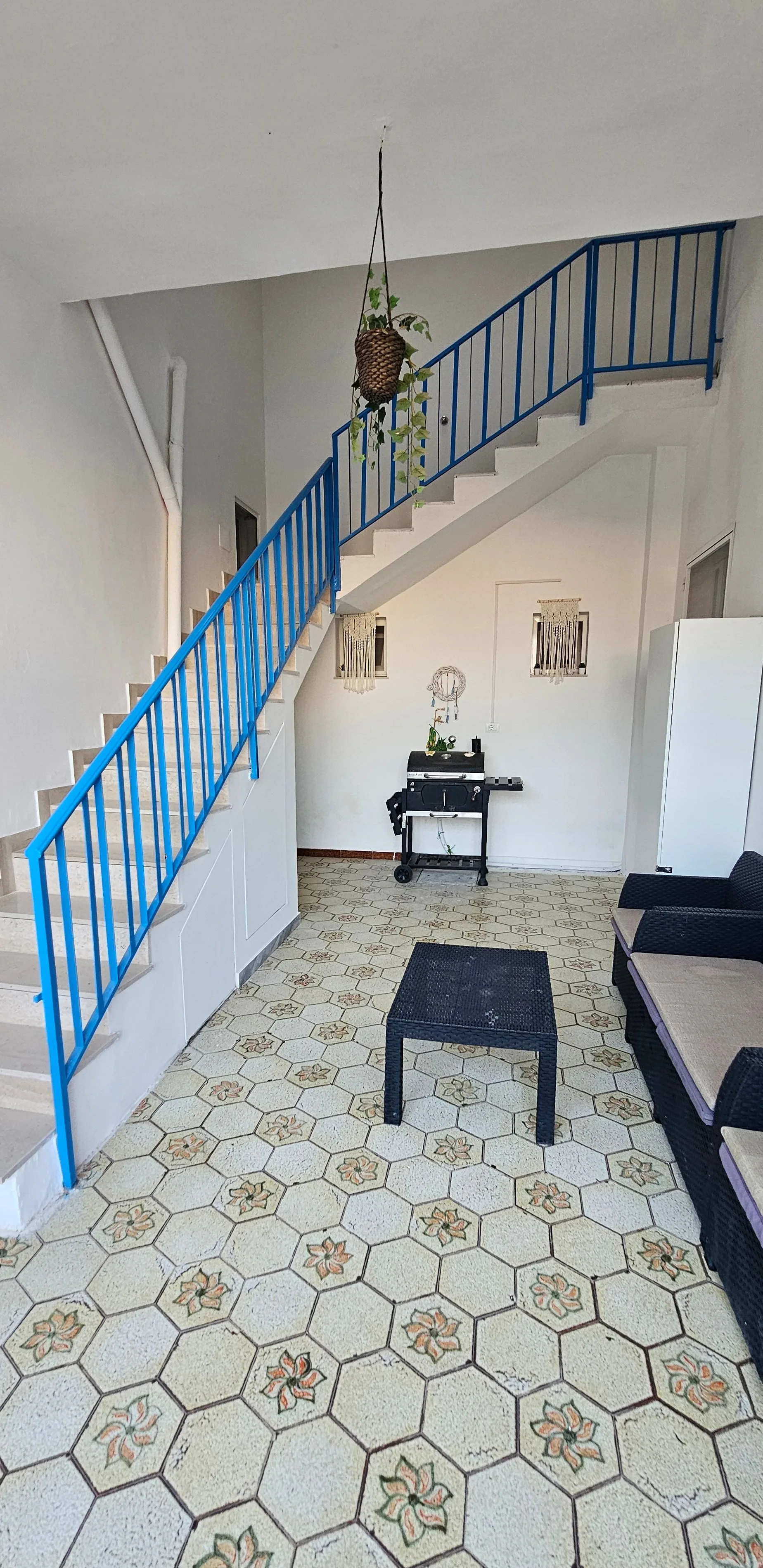 Atrium intérieur avec escalier en fer cobalt et sol en carreaux de ciment à motifs floraux.