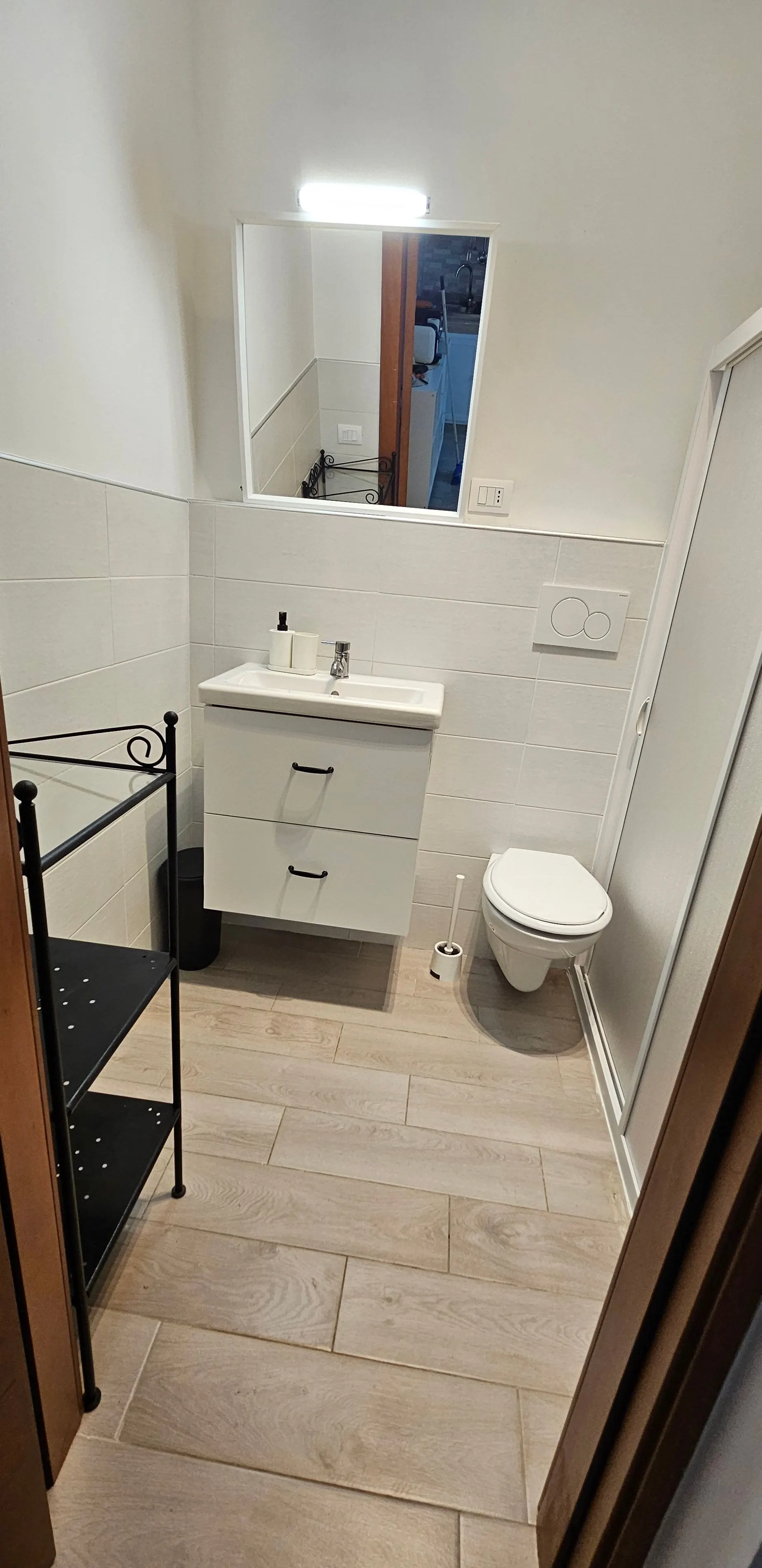 Salle de bain avec lavabo, étagère, sanitaires et sol carrelé effet bois clair.