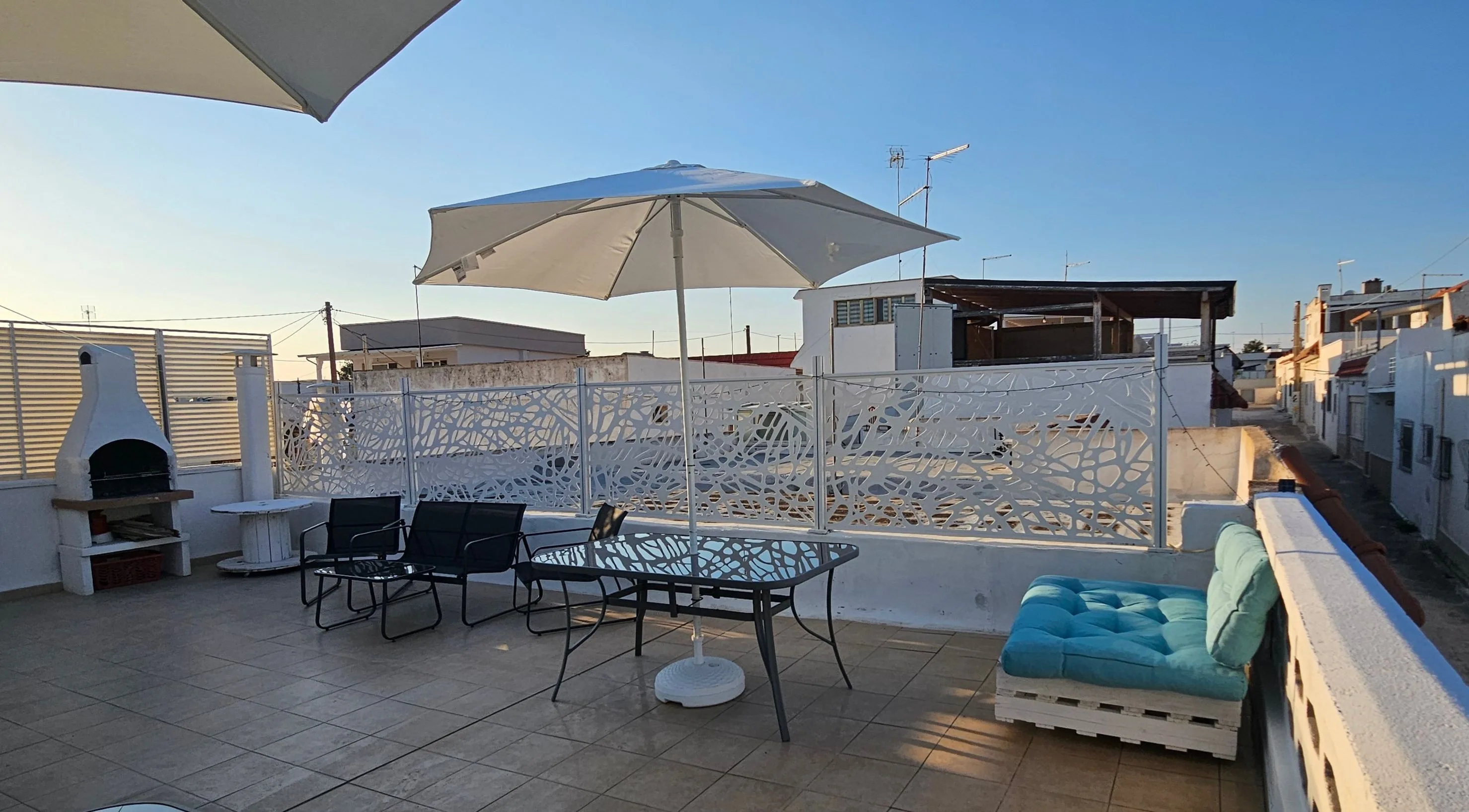 Terrasse avec barbecue en maçonnerie, table sous parasol et canapé en palettes avec coussins bleu clair.