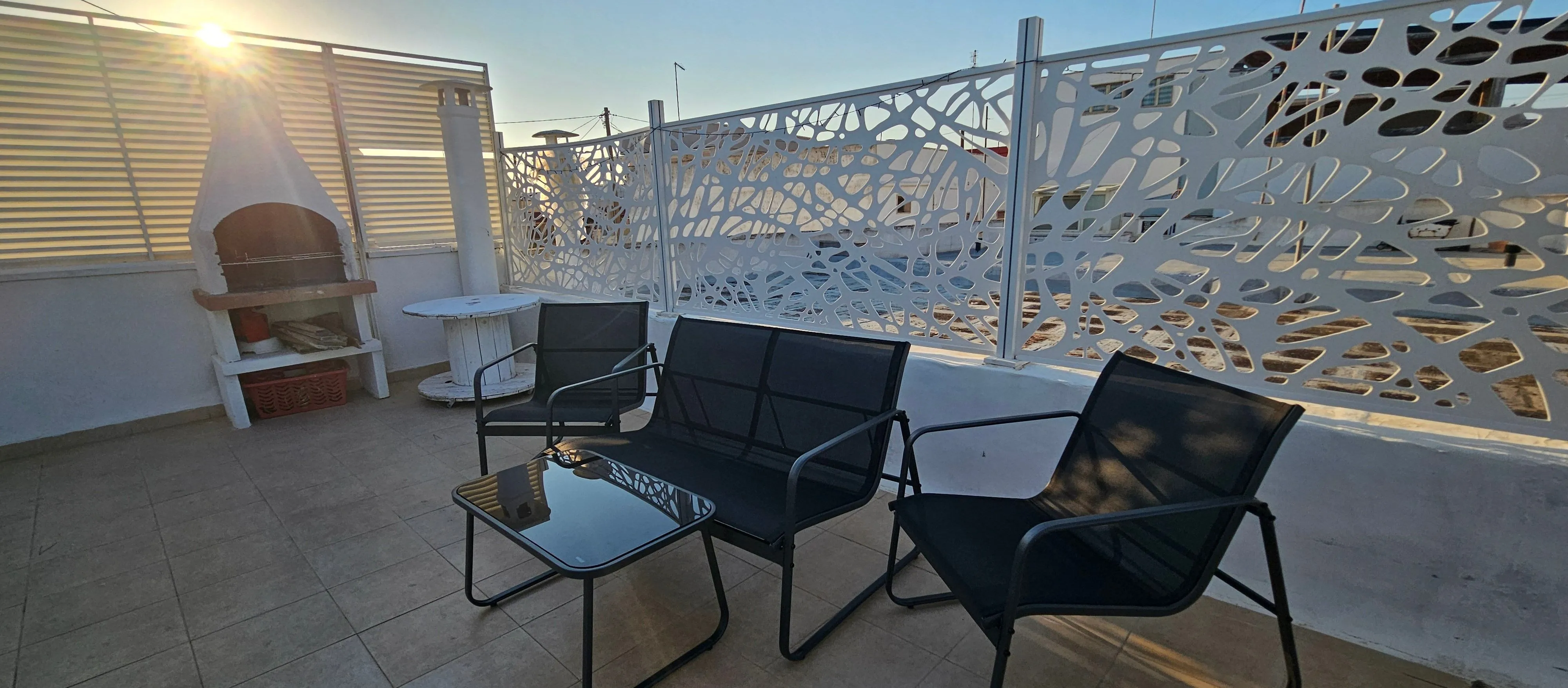 Terrasse au coucher du soleil, canapés de détente au premier plan, lumière chaude à contre-jour.